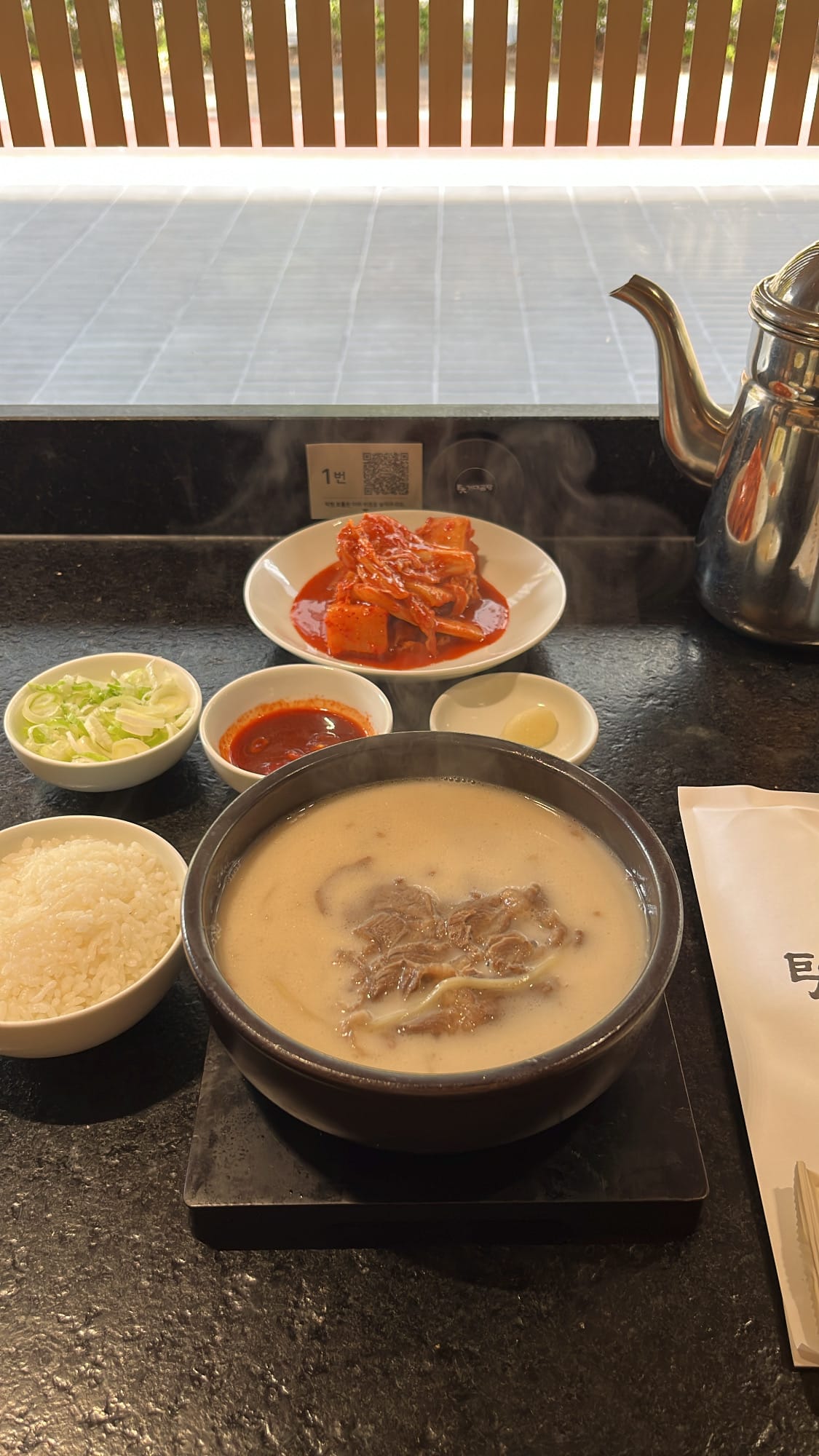 Table setting of Sari Gomtang milky soup served with noodles rice and kimchi at Geodae Gomtang Busan