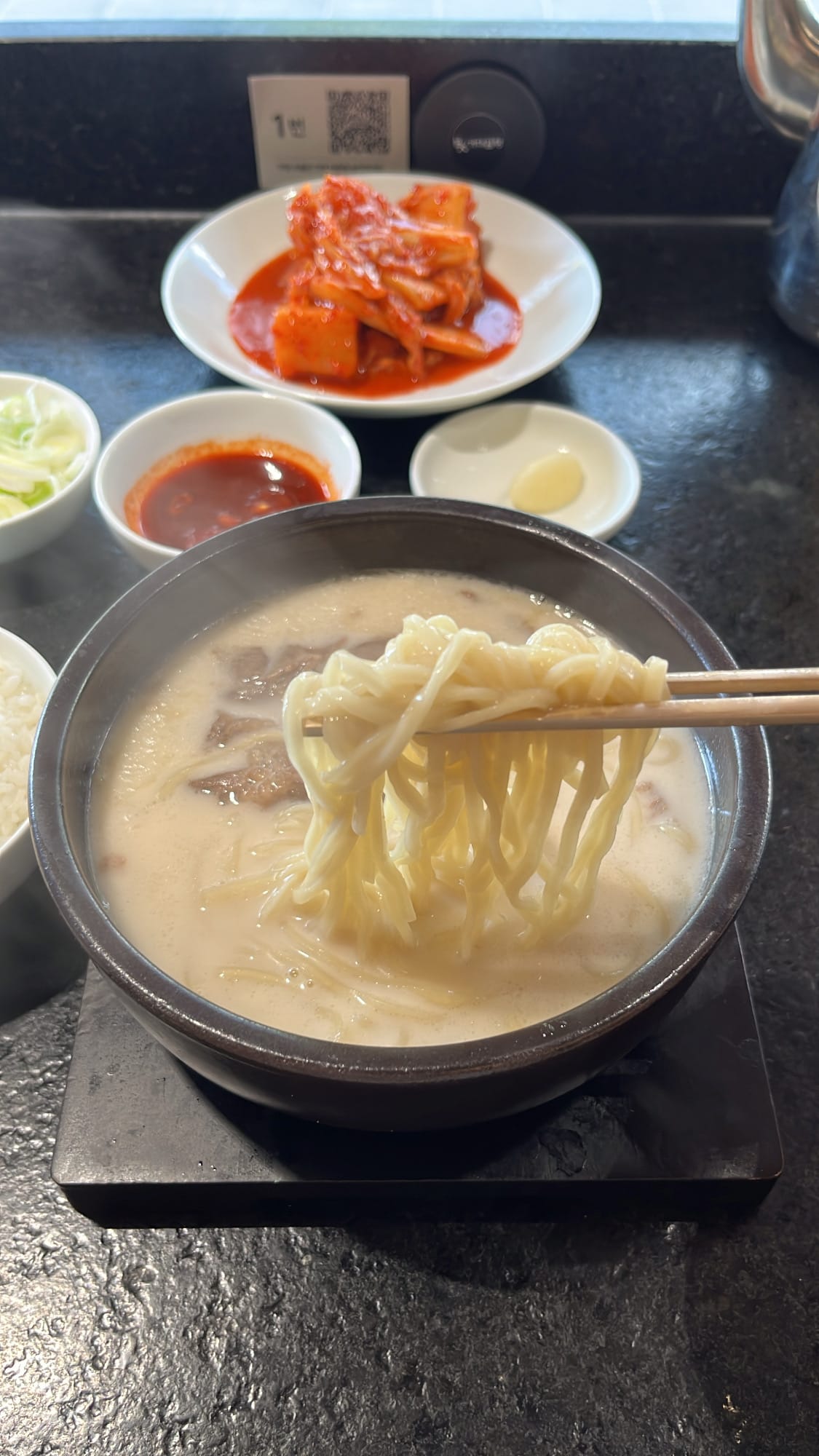 Chopsticks lifting house-made noodles from rich beef bone broth at Geodae Gomtang Busan