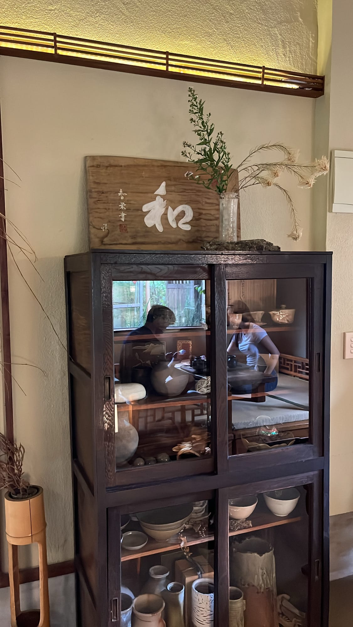 Dark wood display cupboard topped with a harmony calligraphy wooden sign