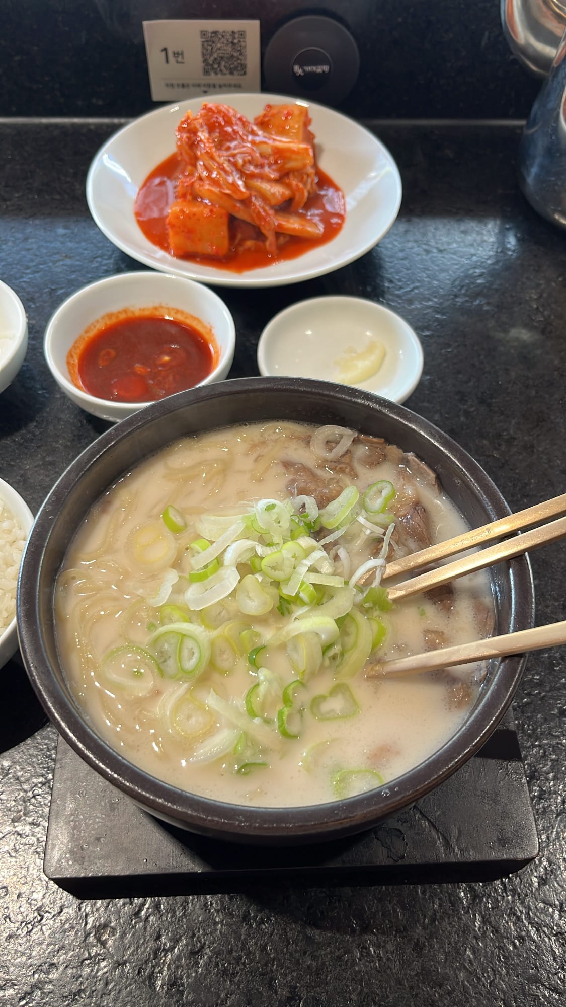 Steaming beef bone soup bowl topped with sliced green onions and garlic paste at Geodae Gomtang Busan