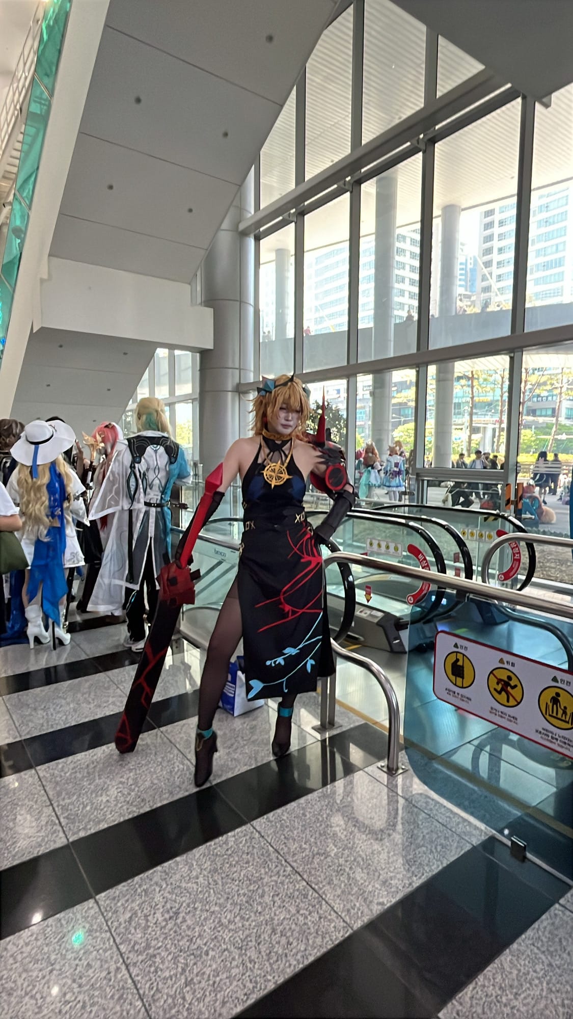 Cosplayer in black dress holding large prop sword inside BEXCO