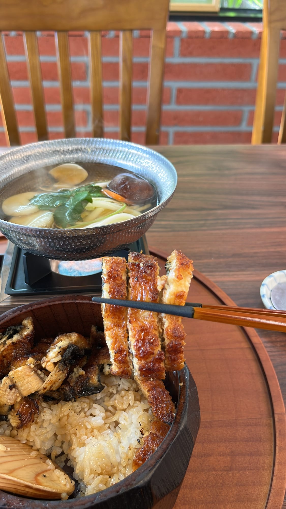 Chopsticks lifting three glossy slices of crisp, glazed grilled eel over rice bowl at Unaju Busan