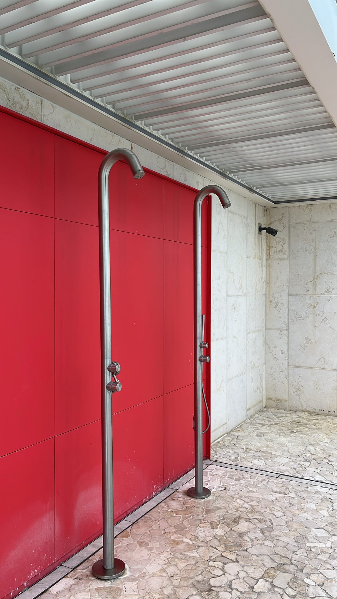 Modern stainless poolside shower posts against bright red wall