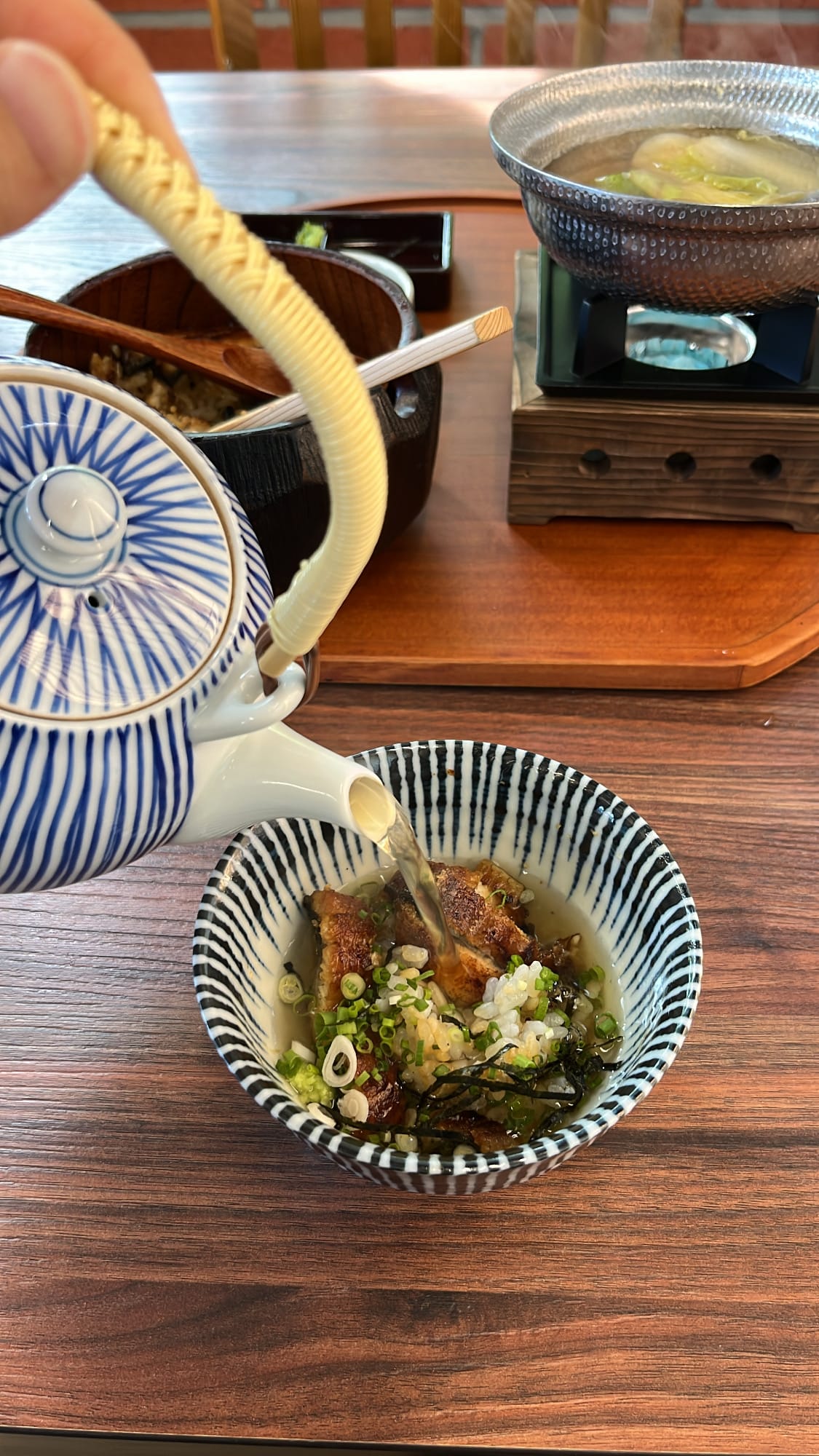 Ceramic teapot pouring warm dashi broth over seasoned eel rice bowl for ochazuke at Unaju Busan
