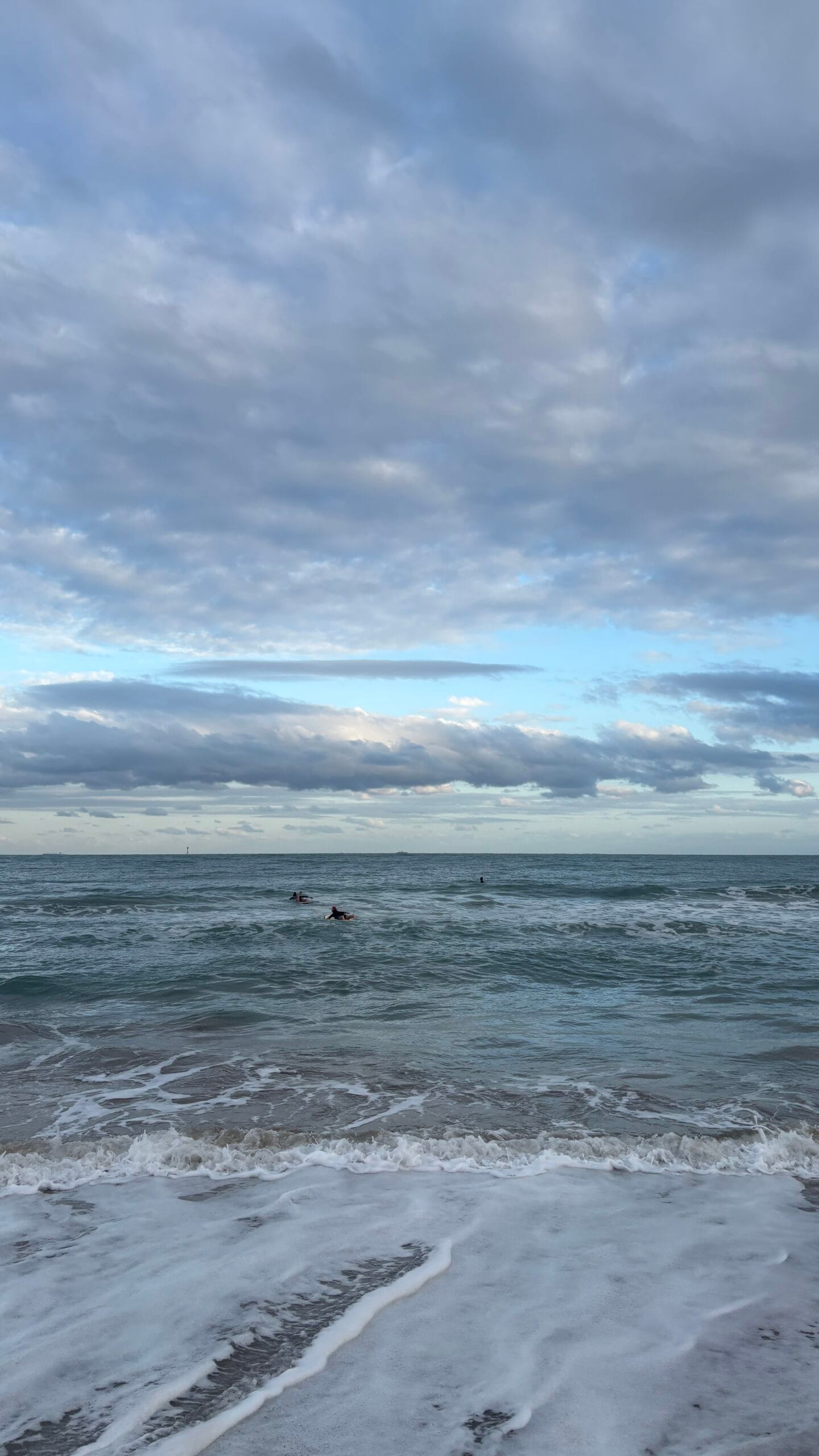 Gentle ocean surf and distant surfers at Songjeong Beach