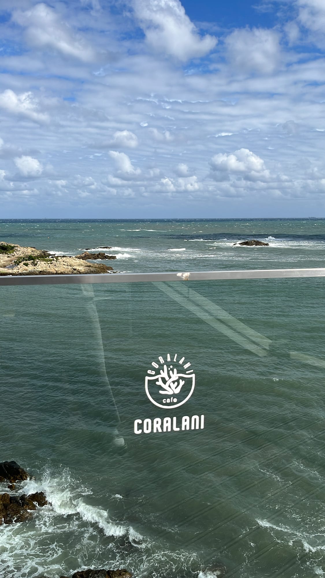 Coralani cafe logo emblem stamped onto transparent glass with crashing waves behind