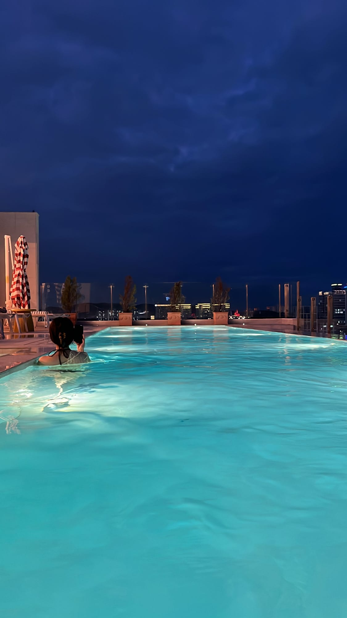 Night infinity pool swim looking out at distant city nightscape